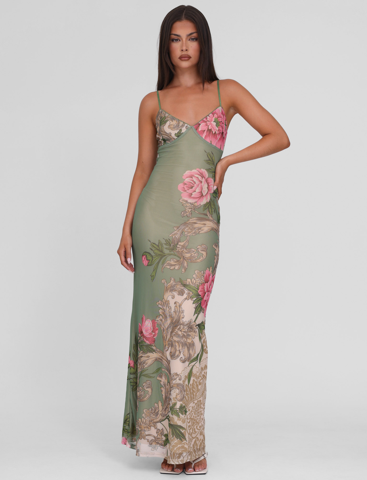 A woman wears the TIGERMIST JULIANNA DRESS in Green Rococo Floral, featuring adjustable spaghetti straps, as she stands against a white background with one hand on her hip.