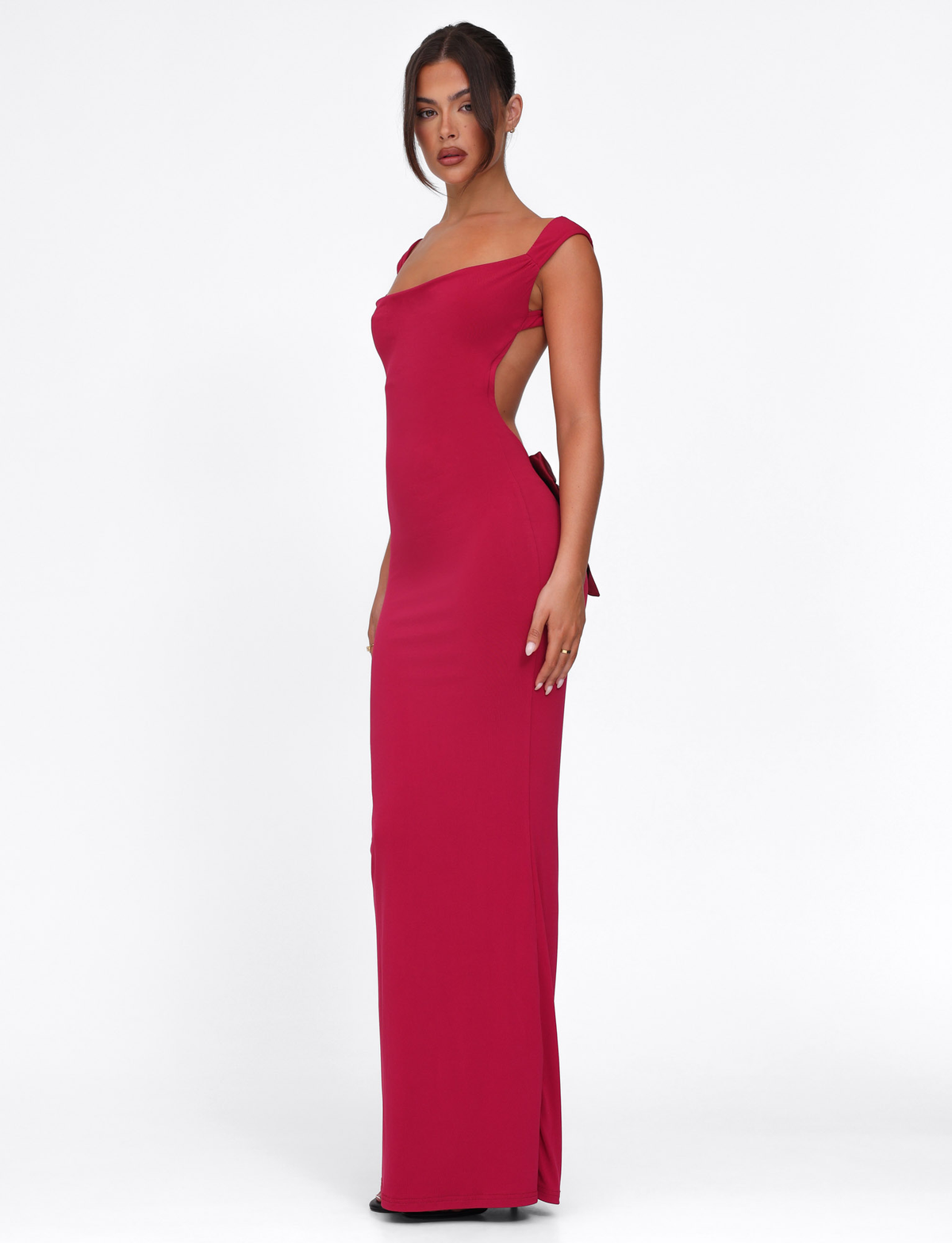A woman poses against a plain white background wearing the TIGERMIST ZITA DRESS in deep red, a fitted, floor-length style with a bodycon silhouette, sleeveless design, open back, and bow detail.