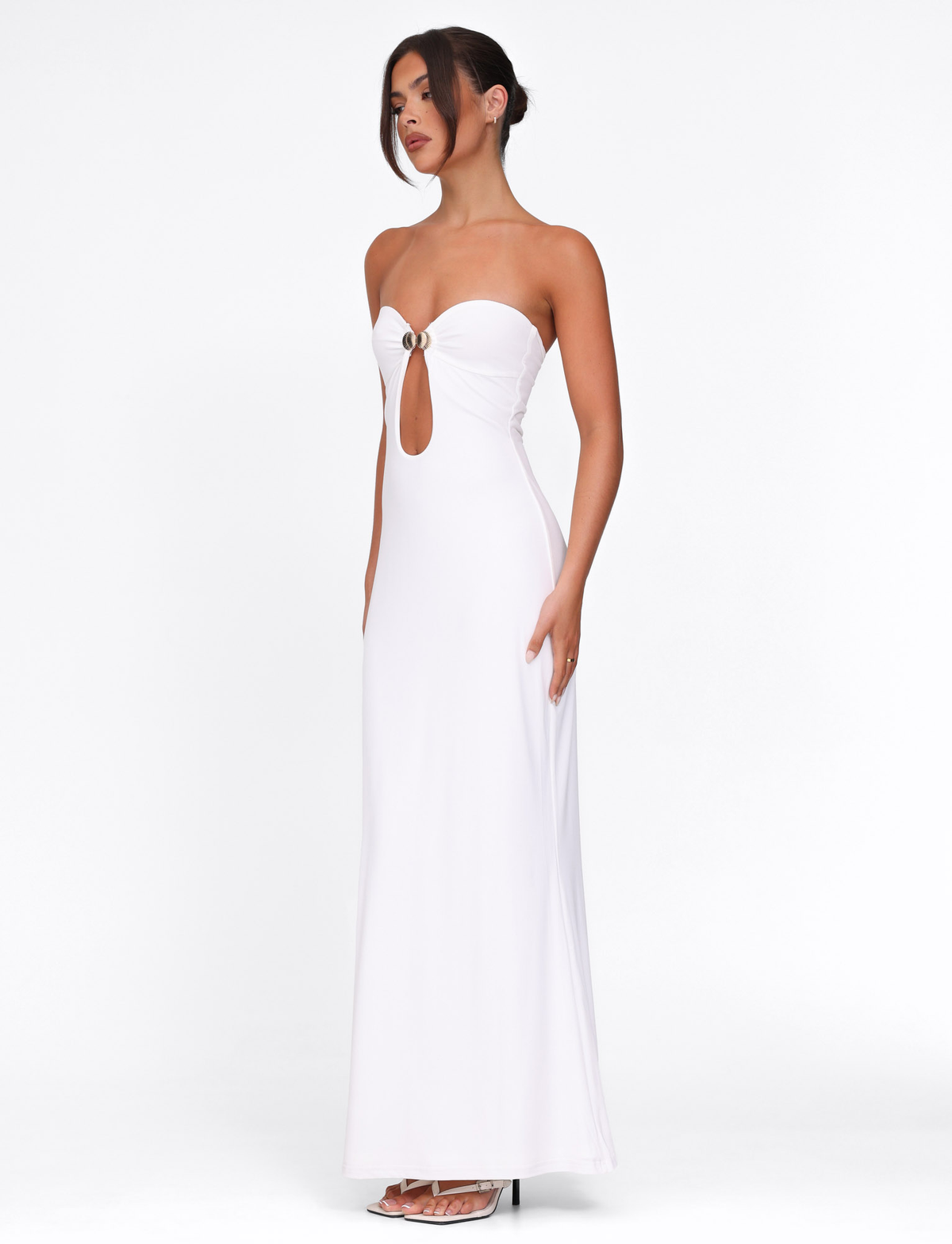 A woman models the TIGERMIST CECILY MAXI DRESS in white, featuring a strapless, sweetheart neckline with a front keyhole cutout and ring detail; she stands in profile with her hair in a low bun against a plain white background.