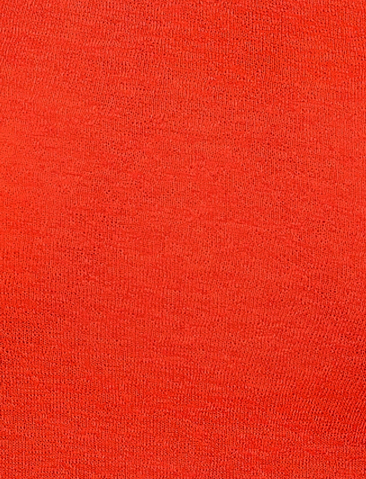 Close-up image of a bright red fabric texture from the BRYNA JUMPER - RED by TIGERMIST, displaying a uniform weave pattern typical of knit fabrication. The surface appears smooth with a slightly visible grain, common in tightly-knit materials like those found in this red sweater. There are no discernible marks, patterns, or variations in color.
