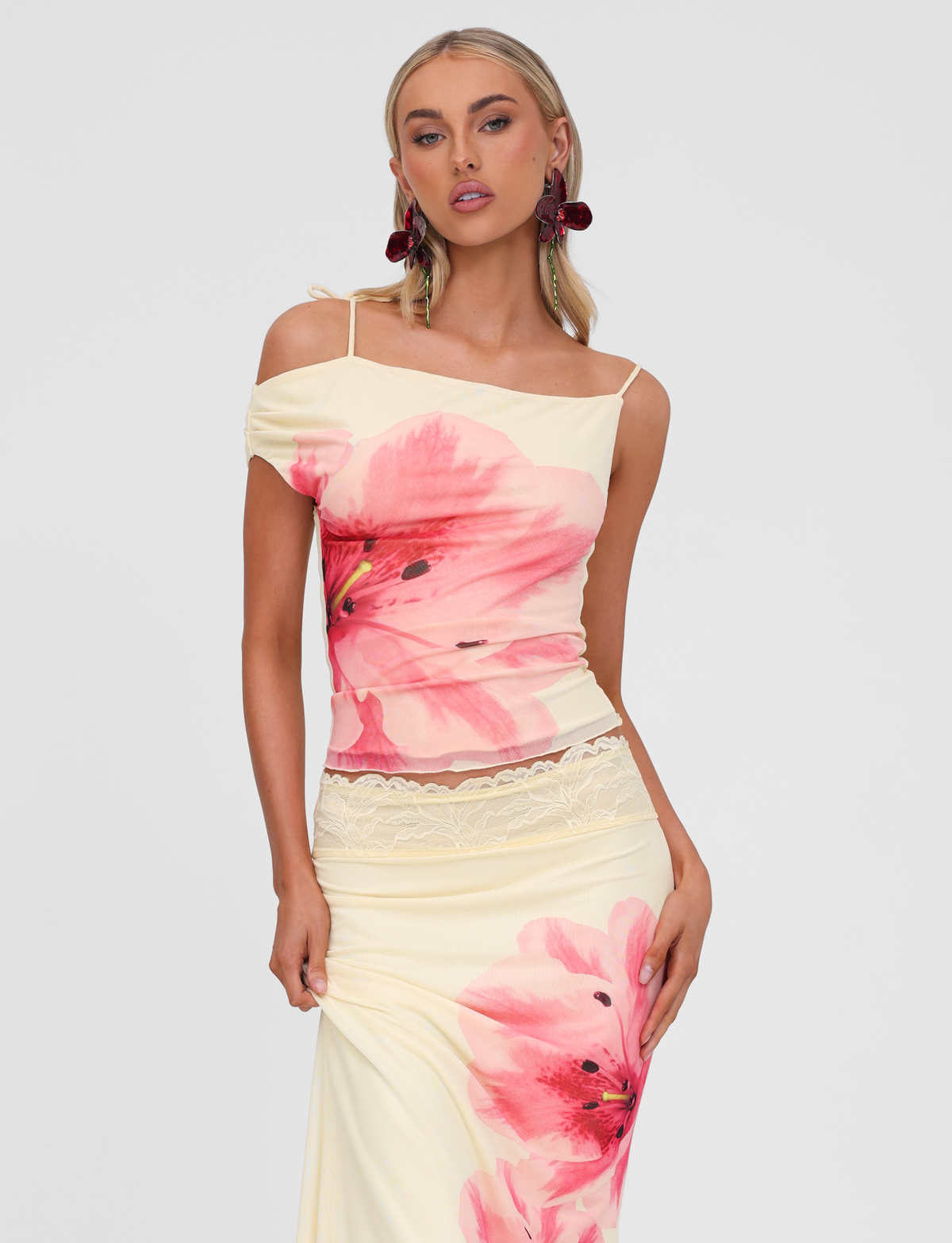 A woman with long blonde hair and statement earrings poses confidently against a plain background, wearing the TIGERMIST LILLIAN TOP in yellow.