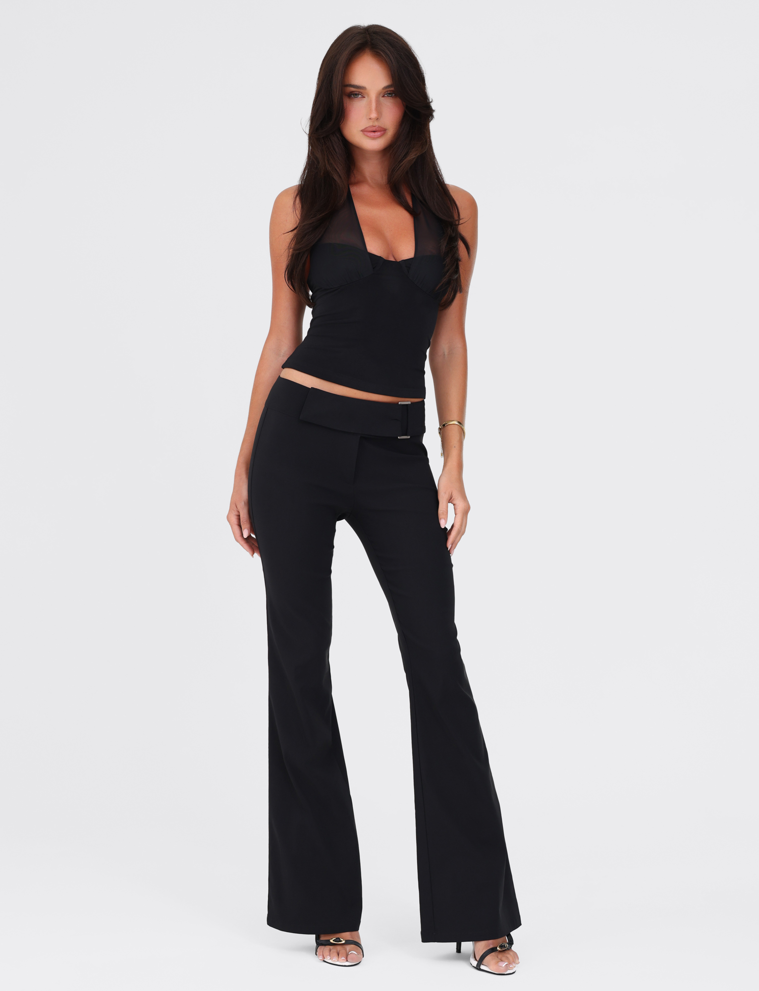 A woman with long brown hair poses confidently against a white background, wearing the TIGERMIST GRANGER TOP in black and black flared pants with heels.