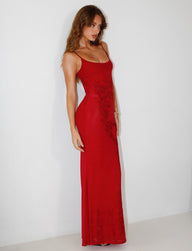 A woman stands against a plain white background wearing the stunning TIGERMIST OCTAVIA MAXI DRESS in cherry red, a long, form-fitting dress adorned with intricate floral embellishments. The elegant design features thin straps, and she poses confidently, her long brown hair cascading over her shoulder.