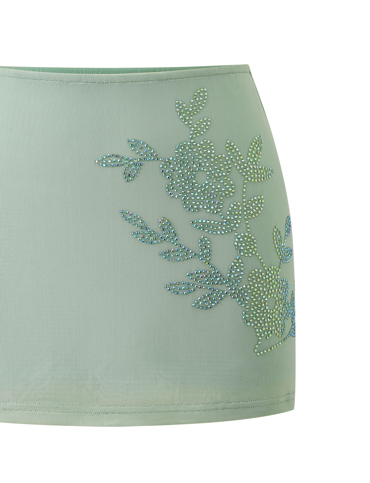 The OCTAVIA MINI SKIRT - PISTACHIO by TIGERMIST is a light green sheer skirt featuring sparkling rhinestone floral embellishment on one side.