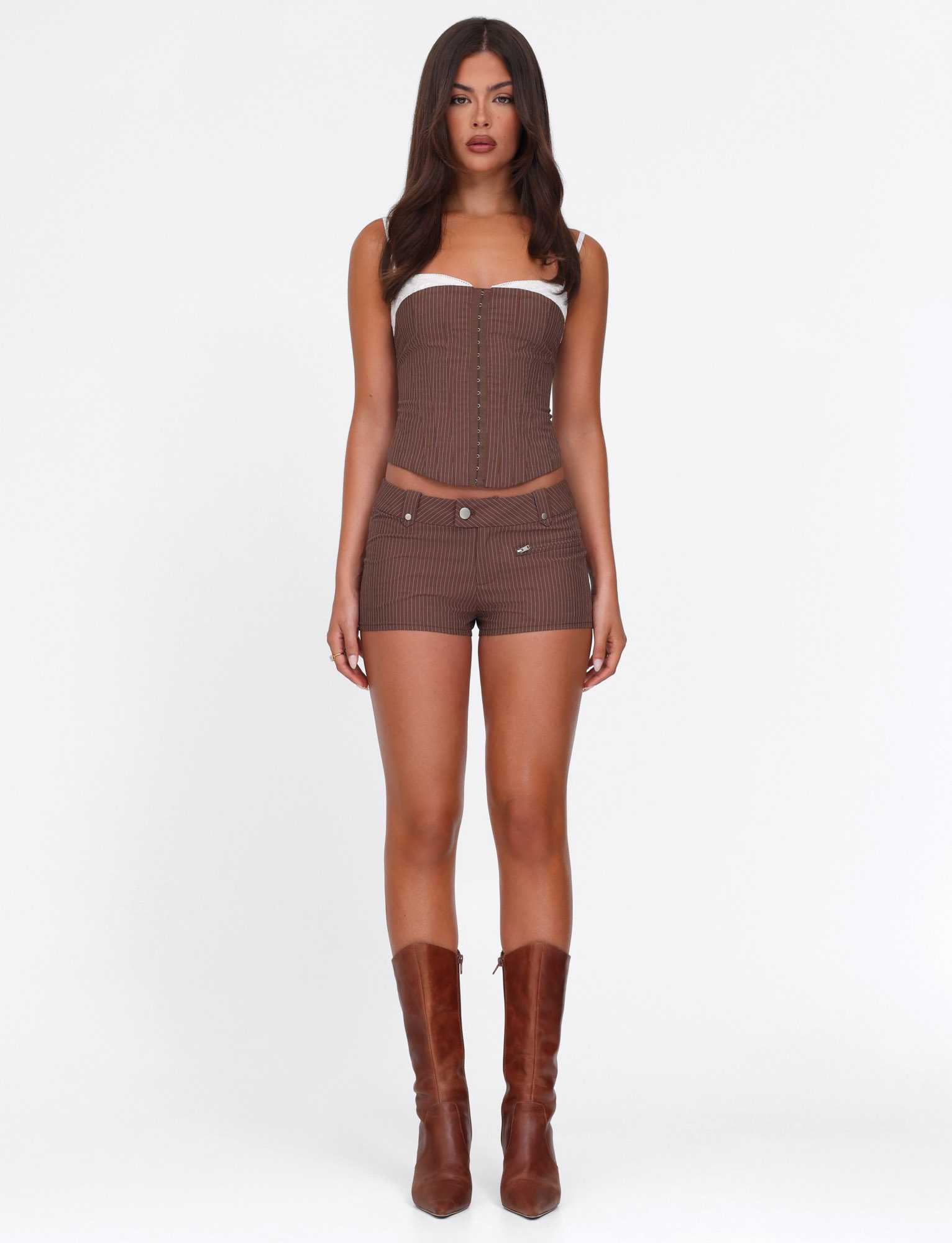 A woman faces forward wearing the TIGERMIST ANTONELLA SHORT in chocolate pinstripe with a matching strapless corset top and knee-high brown boots, posed against a plain white background.
