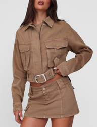 A woman wears the TIGERMIST ZELIE JACKET in washed tan with large patch pockets and silver buttons, paired with a matching mini skirt, set against a plain light background.