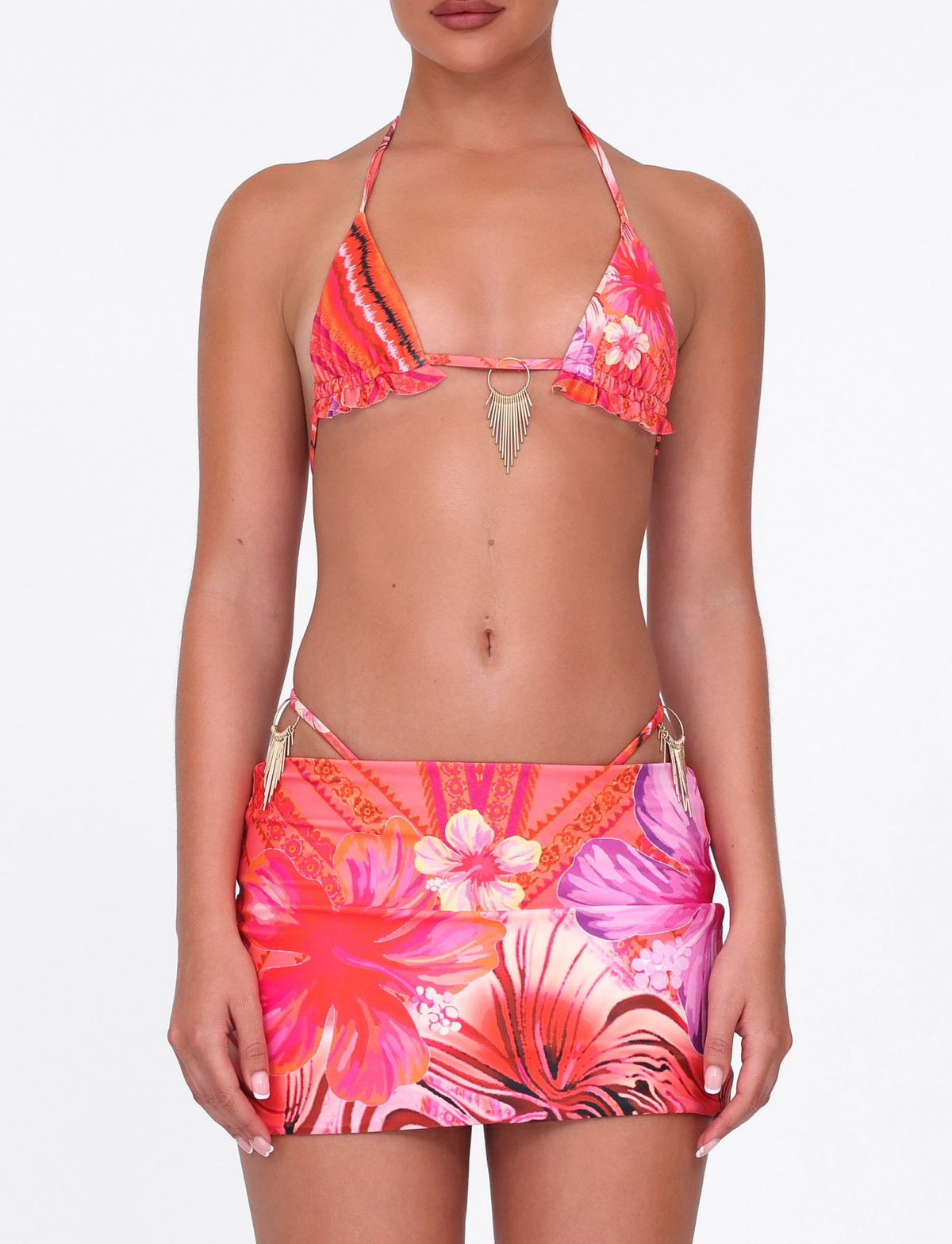 A woman poses confidently against a white background wearing the TIGERMIST CIANA BIKINI 2PC BOTTOM in Pink Tropical Floral with gold ring accents and a matching mini skirt.