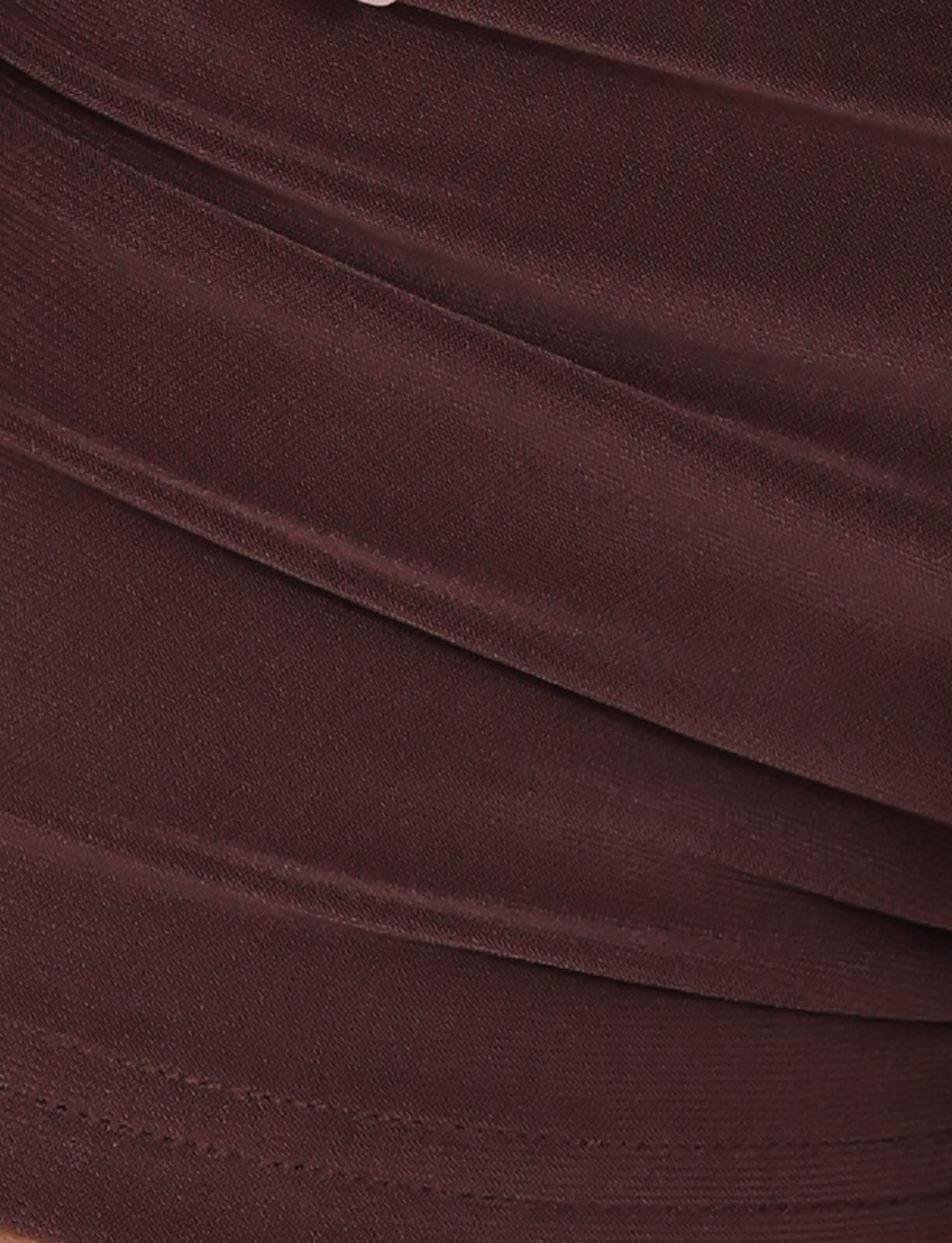 Close-up of chocolate brown fabric with smooth, diagonal pleats and a soft, slightly shiny texture—featured in TIGERMIST's JOVIENNE SHORT - BROWN: CHOCOLATE, perfect for a high-stretch micro mini short.