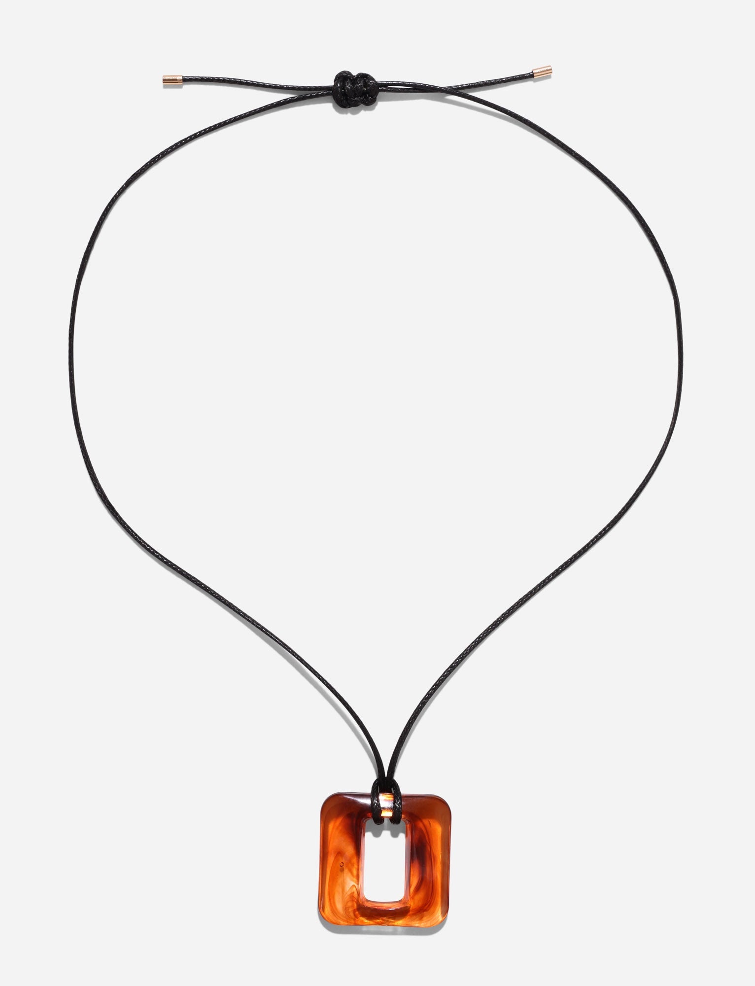 The TIGERMIST MIRREN SQUARE NECKLACE - BROWN, featuring a black woven cord with adjustable length and a striking square amber pendant with a rectangular hole in the center, is elegantly displayed against a plain white background.