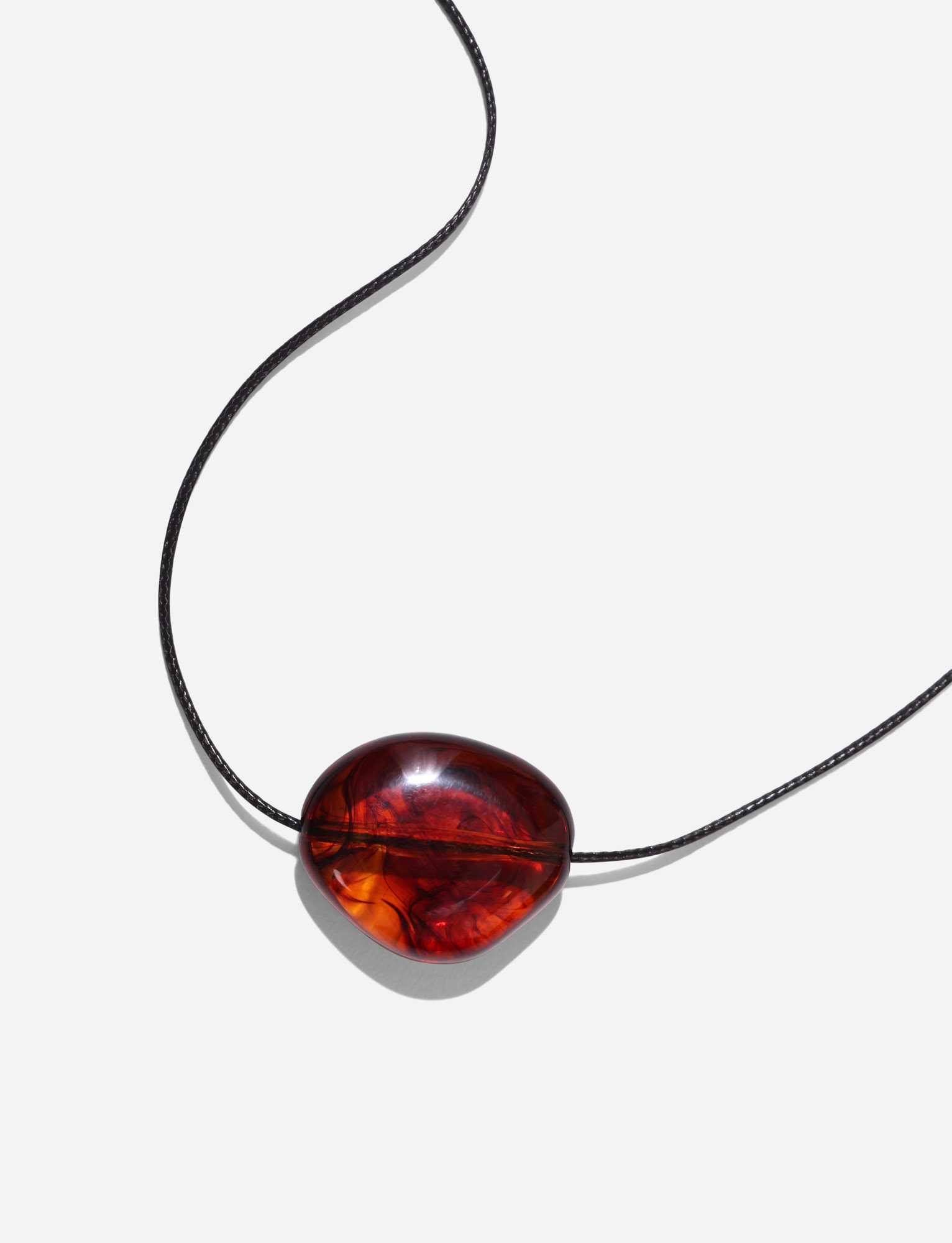 The SOLENE NECKLACE - BROWN by TIGERMIST features a polished, oval amber pendant on a minimalist, adjustable black cord, shown against a plain white background.