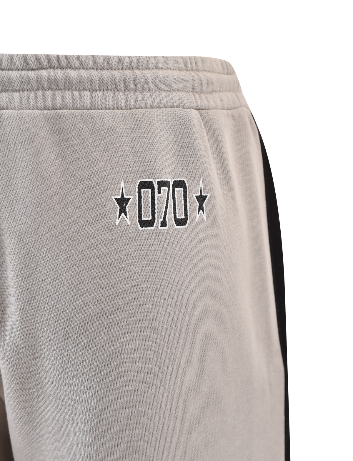 Close-up of TIGERMIST PAYTON TRACKPANT - STONE: grey trackpants with black "070" outline and star accents near the pocket, plus a sporty black side stripe.