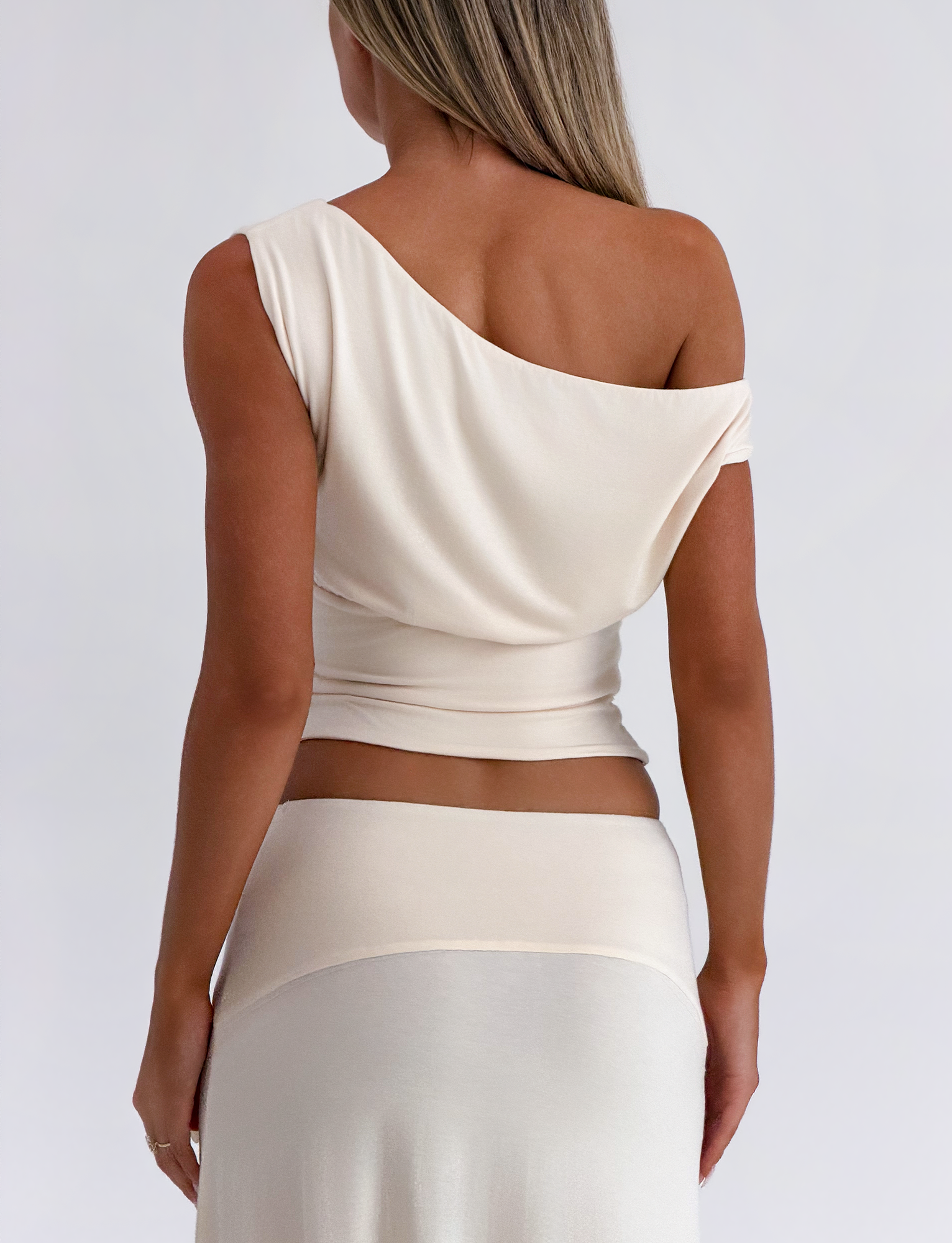 A woman with long, straight blonde hair is seen from behind in the TIGERMIST ALYSSA OFF SHOULDER TOP - CREAM and a matching skirt, highlighting her elegant silhouette against a plain, light backdrop.