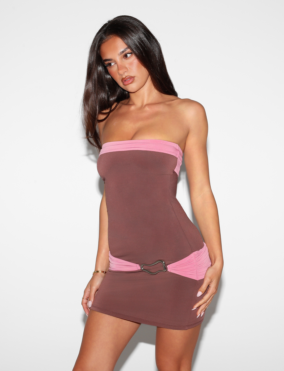 A woman with long dark hair wears the Tiger Mist USA CL - EOS MINI DRESS, a strapless brown mini dress with pink accents, posing against a plain white background.