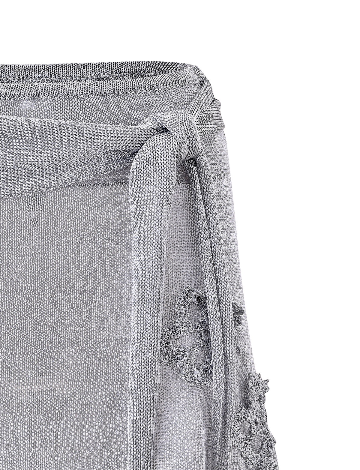 Close-up of the TIGERMIST ISATANA MINI SKIRT - SILVER, featuring light gray sheer metallic knit fabric, a textured waist tie bow, and decorative floral lace patterns on the side.