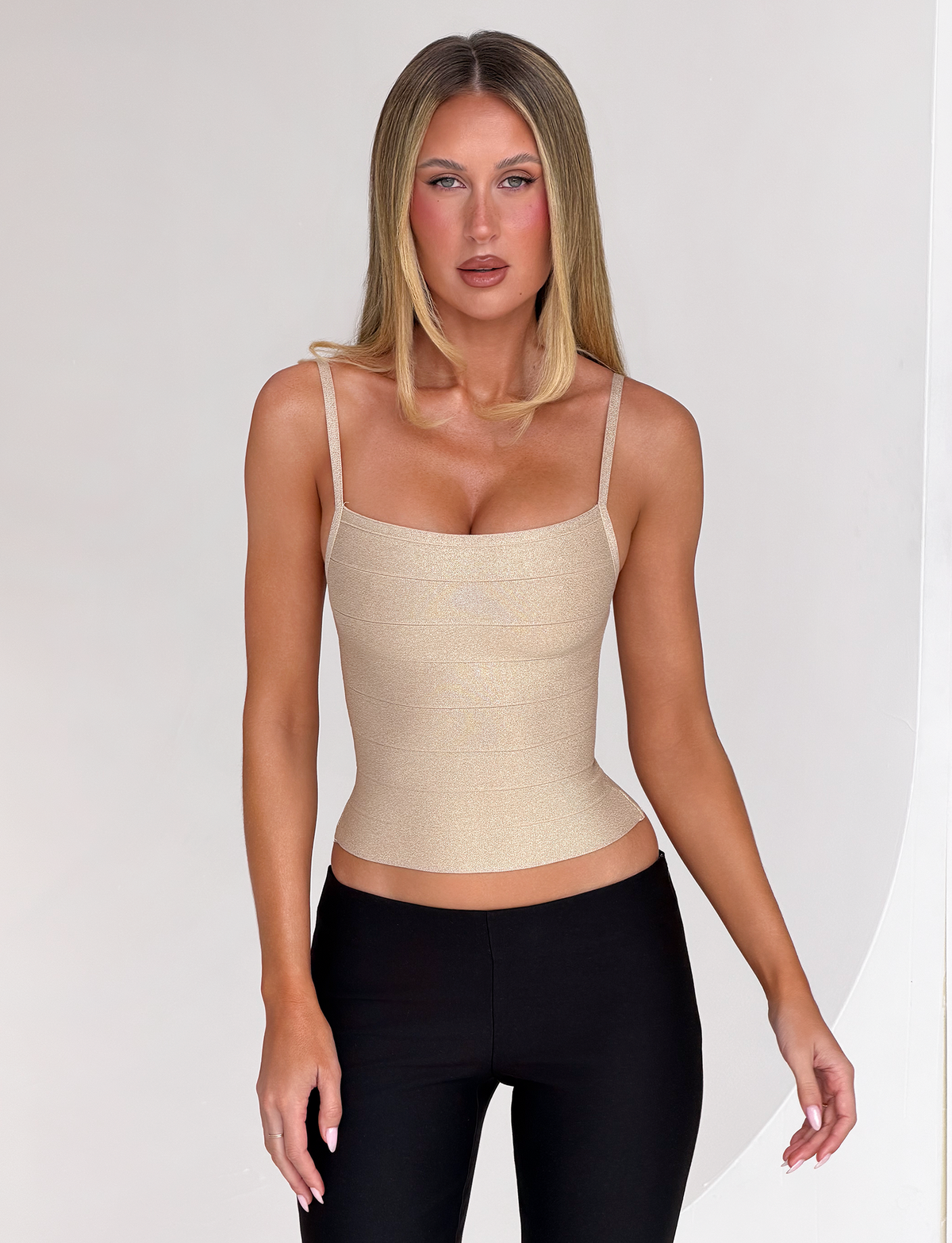 A person wearing a sparkly gold MIDORI BANDAGE TOP with a square neckline, spaghetti straps, and black trousers.
