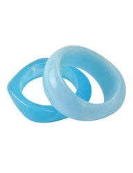 The MIKAH BANGLE SET - AQUA by TIGERMIST features two chunky, organically shaped blue acrylic bangles—one darker and angular, the other rounder and lighter—overlapping on a white background.
