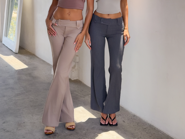 Close up of model wearing black suit pants an white top standing against a white wall