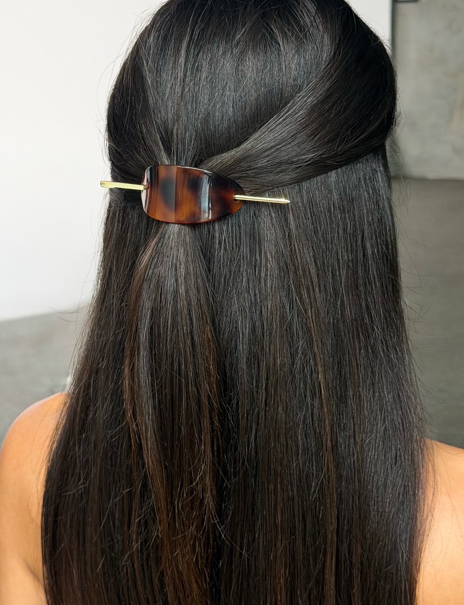A person with long, straight, dark hair styled half-up wears the chic TIGERMIST RUKA BARETTE in tortoiseshell. The background is minimal and neutral.