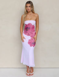 A woman with long blonde hair is wearing the LILLIAN DRESS - PINK by TIGERMIST, a strapless, form-fitting white midi dress featuring large pink floral designs. She poses against a plain beige background and completes the look with white open-toe heels.