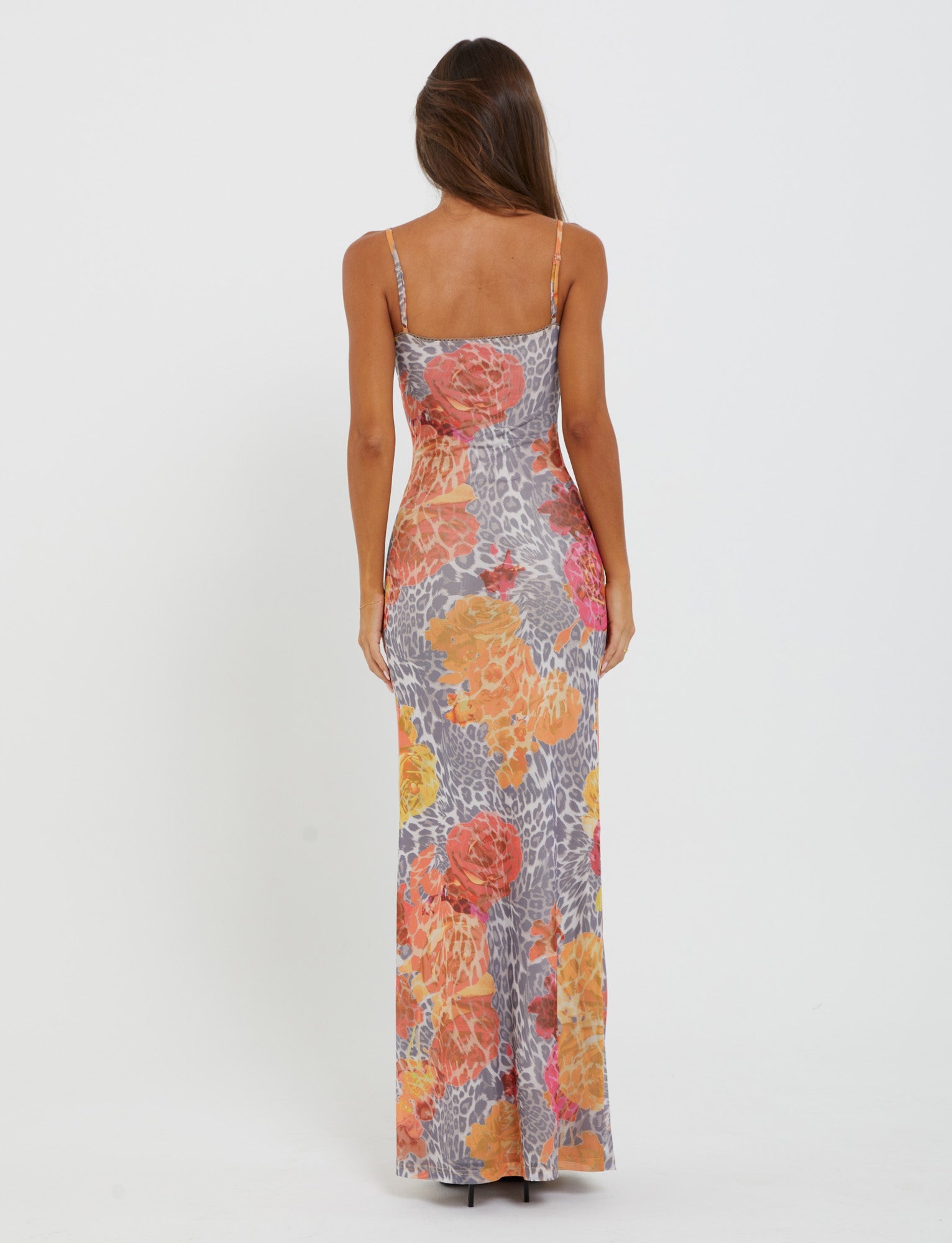 A person with long, brown hair is wearing the sleeveless ankle-length JULIANNA DRESS from TIGERMIST, featuring a vibrant multi-color print with leopard and orange leopard patterns. They are standing with their back to the camera against a plain white background.