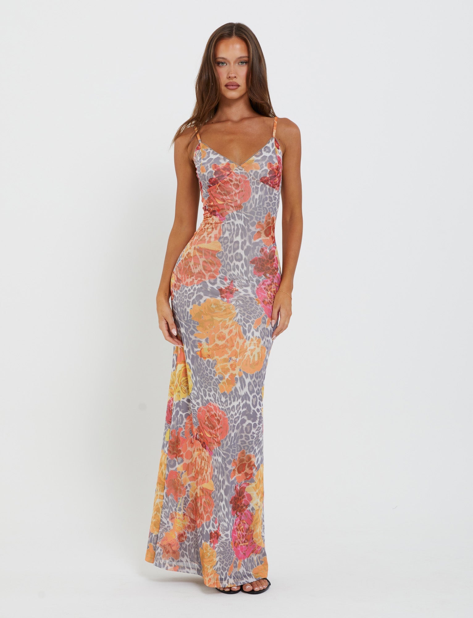 A woman stands against a plain white background wearing the form-fitting, sleeveless JULIANNA DRESS - MULTI : LEOPARD : ORANGE LEOPARD by TIGERMIST. The dress features a vibrant floral and animal print in orange, yellow, and gray tones. She has long, straight hair and is looking directly at the camera.