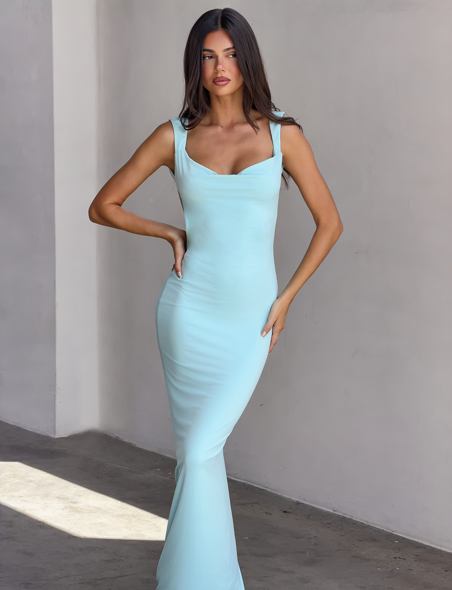 A woman wears the TIGERMIST MORANA DRESS in sky blue, featuring a scoop cowl neck and maxi length.