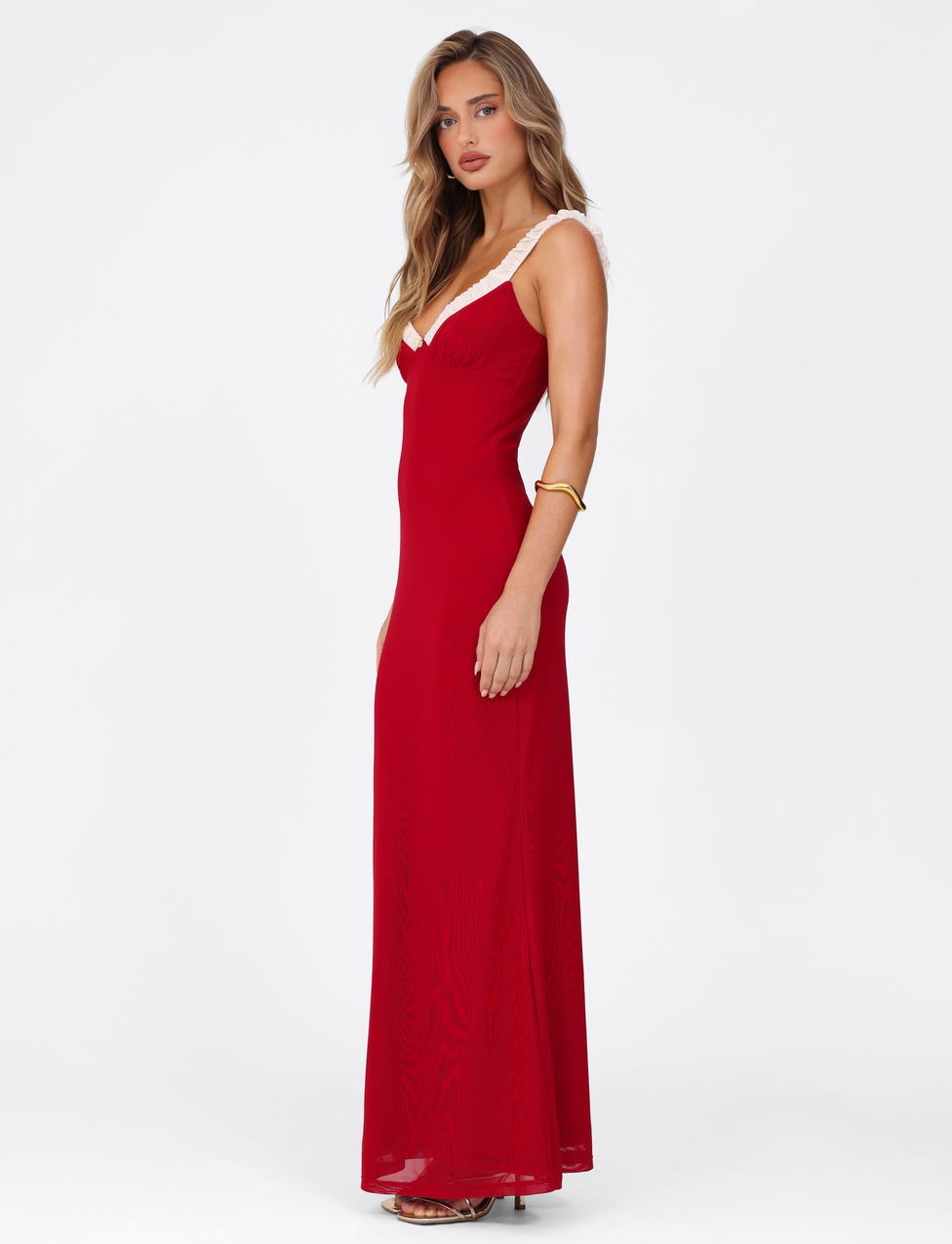 A woman with long, wavy blonde hair wears the TIGERMIST AMARAN MAXI DRESS - RED : BURGUNDY, a long bodycon style with white strap trim, accessorized with a gold bangle and posing against a plain white background.