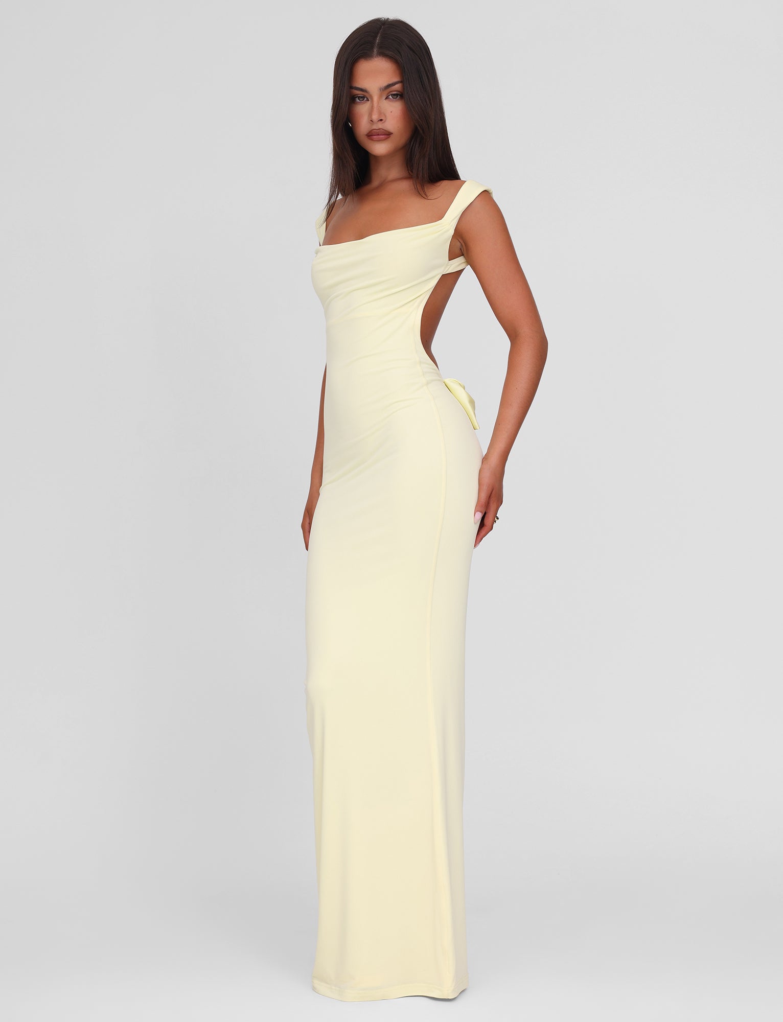 A woman poses in the TIGERMIST ZITA MAXI DRESS - LEMON featuring off-the-shoulder straps, a bodycon fit, and an open back, set against a plain light grey background.