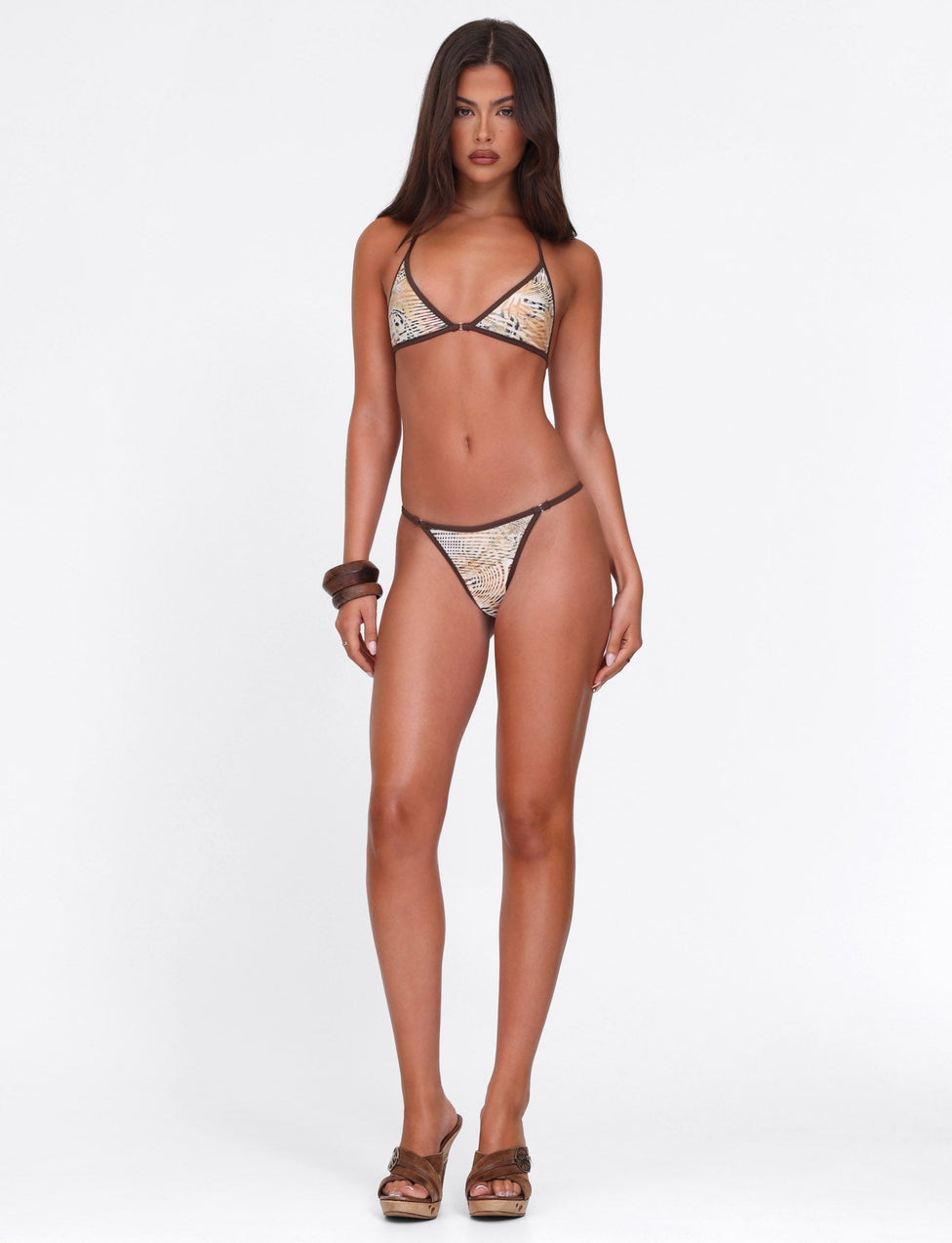 A woman with long brown hair and minimal jewelry wears the TIGERMIST DIANA BIKINI TOP in ANIMAL MARBLE against a white background, paired with brown wedge sandals and a neutral expression.