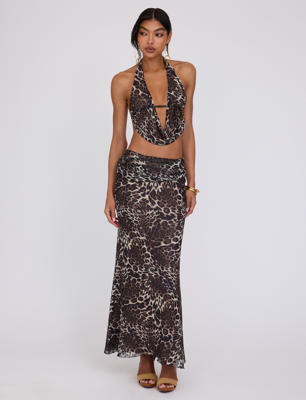 A woman models the TIGERMIST PEARL MAXI SKIRT - MULTI : LEOPARD, a maxi silhouette with a brown and black leopard print, paired with a sleeveless crop top, gold heels, and gold jewelry against a plain white background.