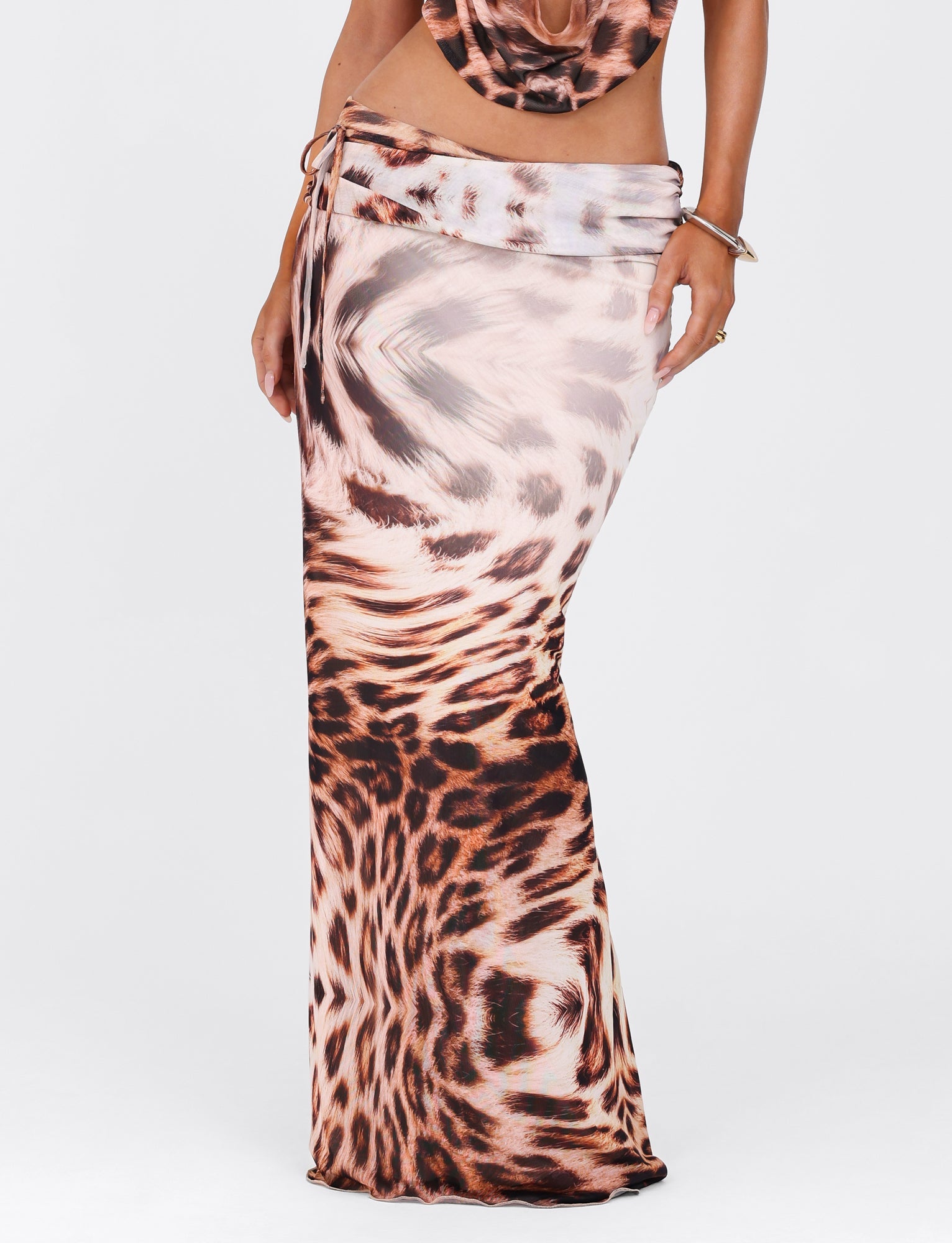 A person dressed in the TIGERMIST Pearl Maxi Skirt - Neutral Leopard Haze. This long, form-fitting skirt showcases a relaxed silhouette featuring a wrap-around design and tie at the waist, set against a plain light background.