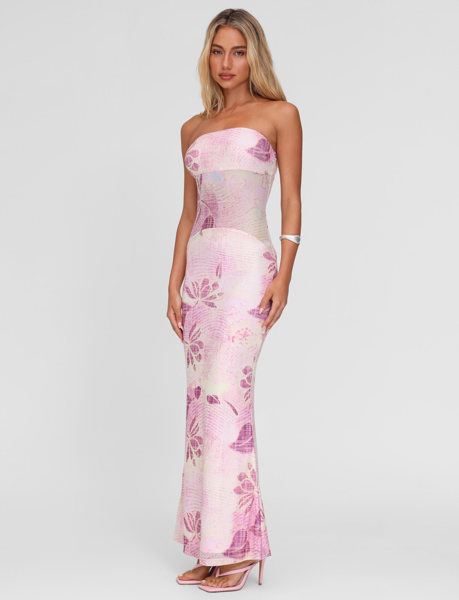 A woman wears the TIGERMIST MORGAN MESH DRESS in Grunge Floral Magenta, featuring a strapless neckline, as she stands in heels against a plain white background.