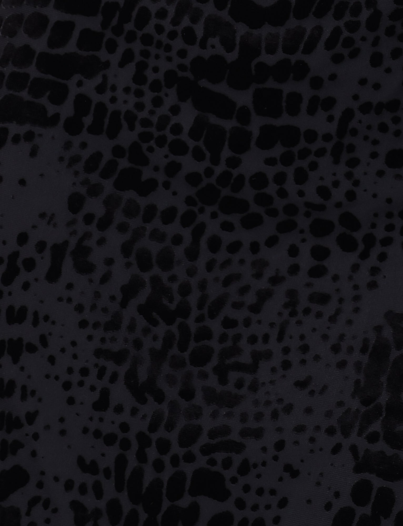 The ALLIRA BURNOUT MINI DRESS 2.0 by TIGERMIST features a black surface with an abstract pattern of irregular, splotchy dark spots that resemble an animal print or a textured material, evoking the look of a velvet burnout design akin to a snake pattern.
