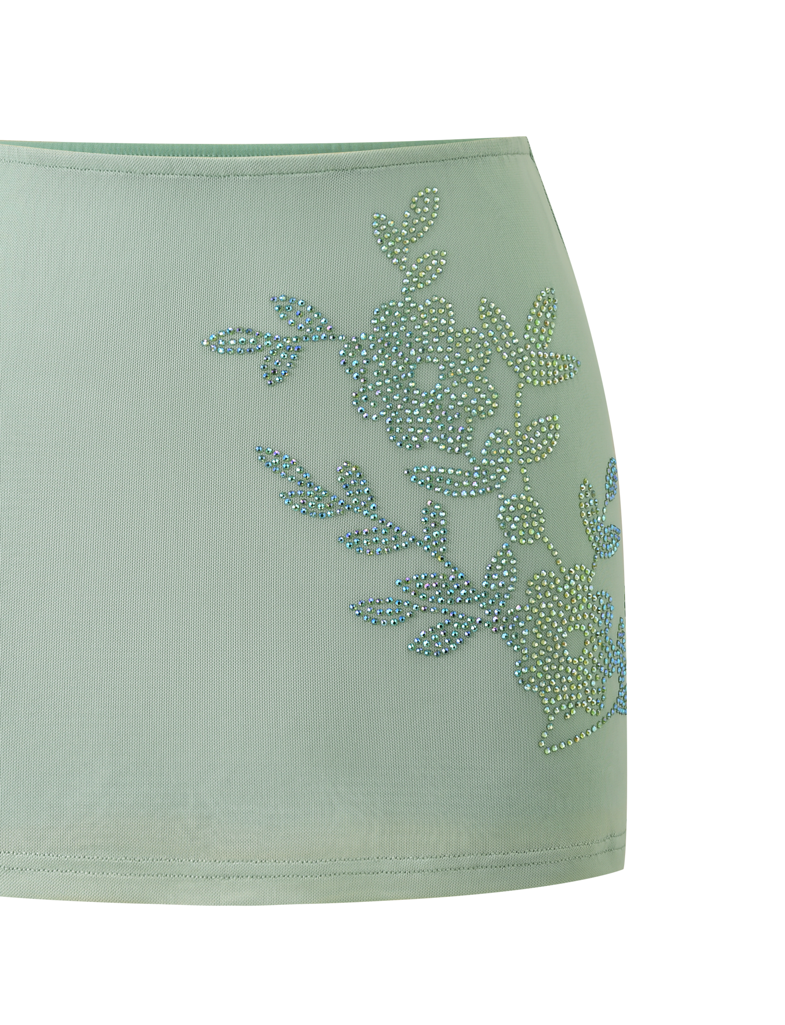 The OCTAVIA MINI SKIRT - PISTACHIO by TIGERMIST is a light green sheer skirt featuring sparkling rhinestone floral embellishment on one side.