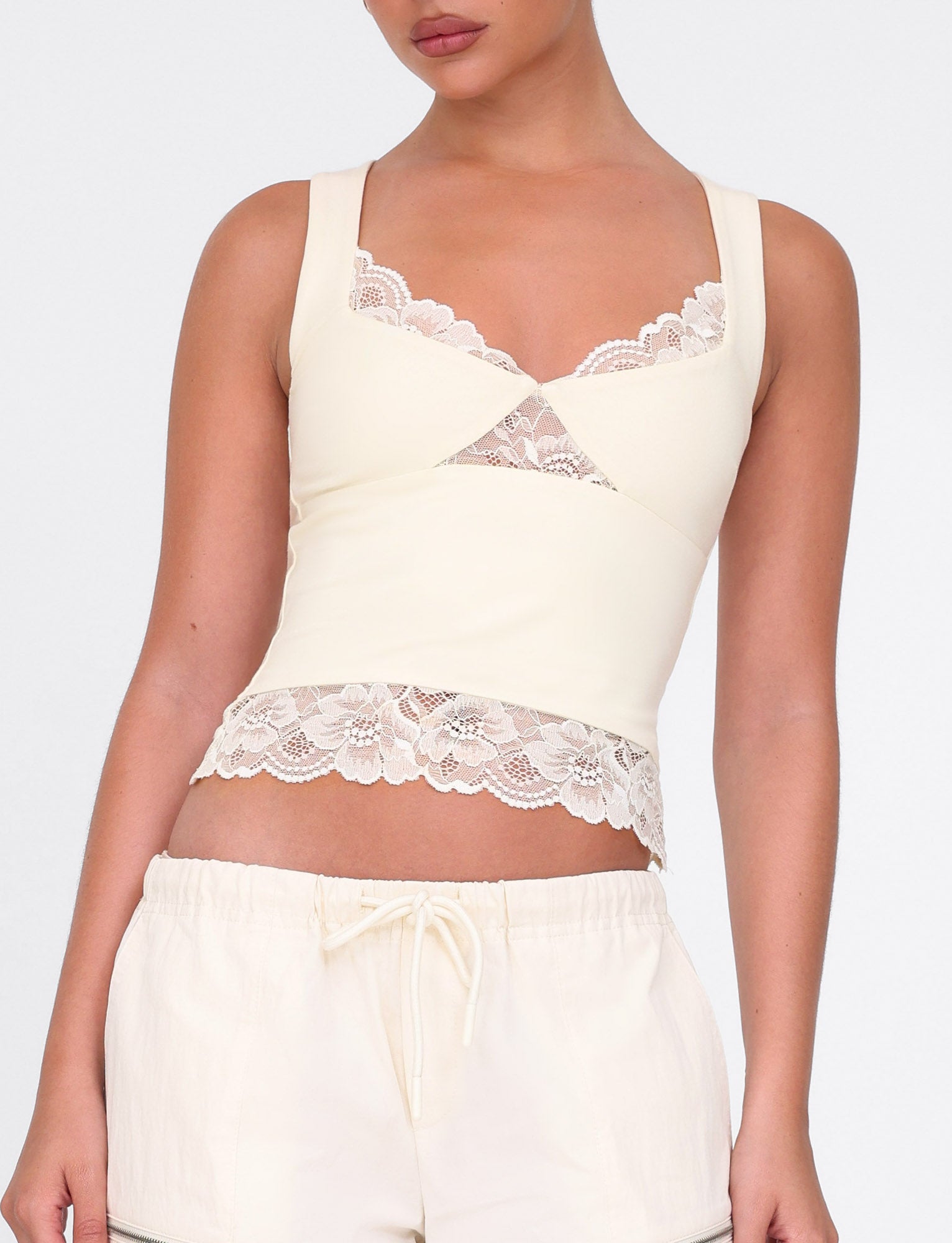 A person wearing a yellow sleeveless DIONE LACE TOP by TIGERMIST, crafted from a soft butter jersey with lace details at the neckline and hem, paired with matching loose-fitting pants featuring a drawstring waist, creating a casual yet elegant look.