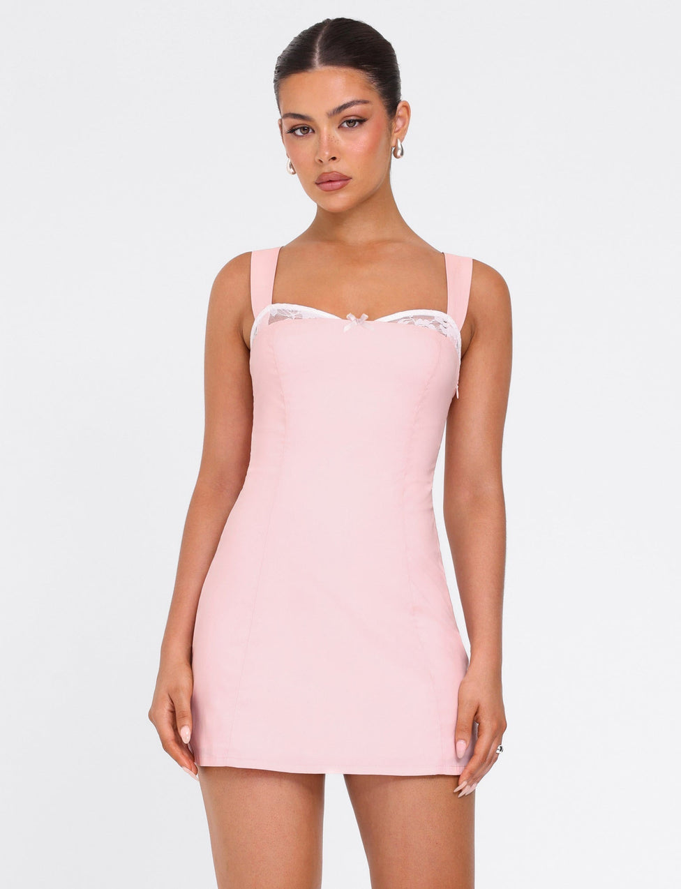A woman models the Tiger Mist USA CL - COLSON MINI DRESS, a fitted light pink mini dress with wide straps and white lace trim at the neckline, standing against a plain white background.