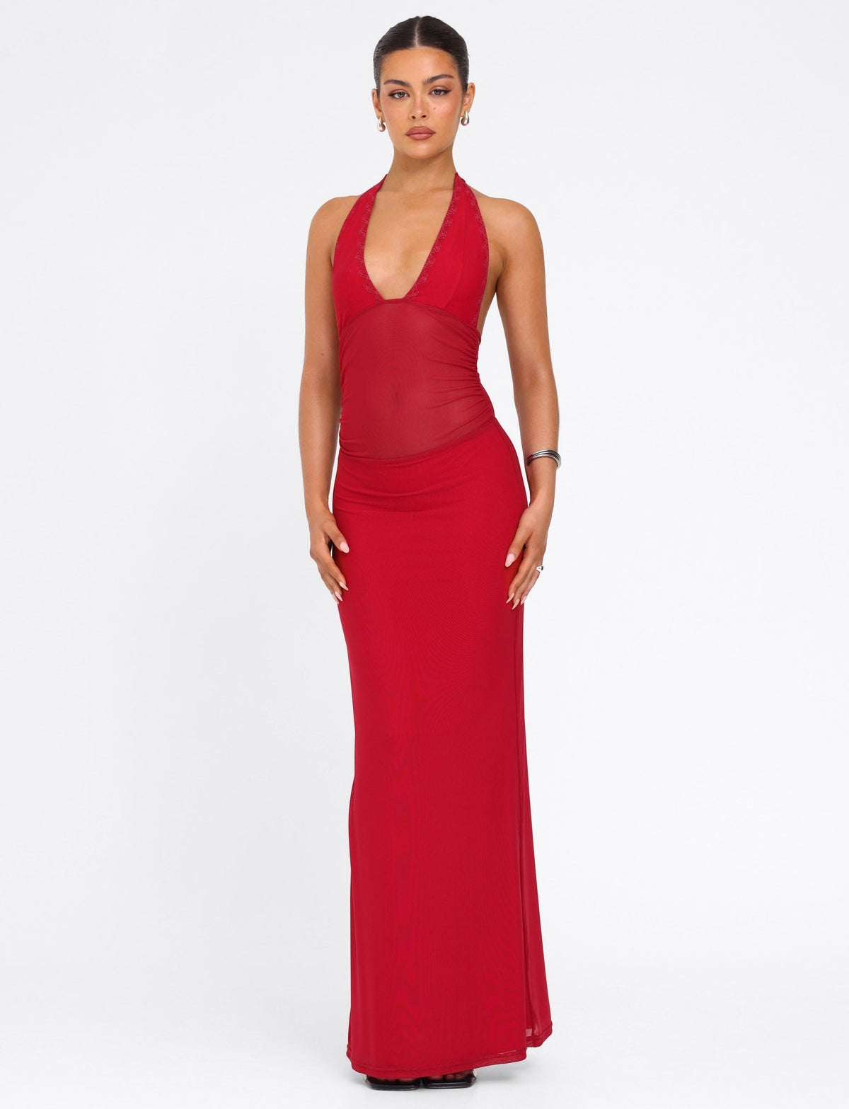 A woman poses against a white background wearing the TIGERMIST BRESILY MAXI DRESS in red, featuring sleeveless tie halter straps, a deep neckline, and sheer embroidered details, accessorized with earrings and a bracelet.