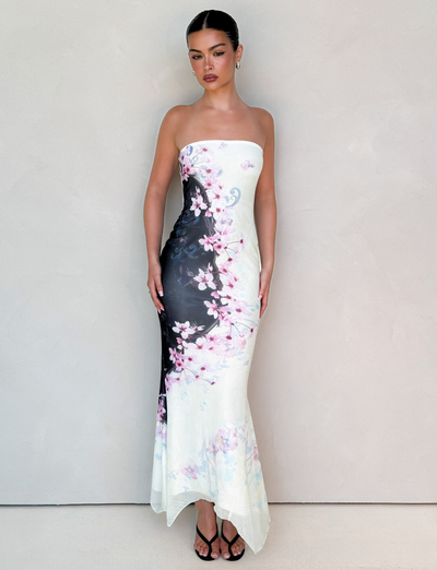 A woman stands against a light beige wall wearing the TIGERMIST LILLIAN MAXI DRESS in Multi Floral Cherry Blossom, a strapless mesh piece with black and white gradient. Her hair is pulled back, and she completes the look with black open-toe heels.