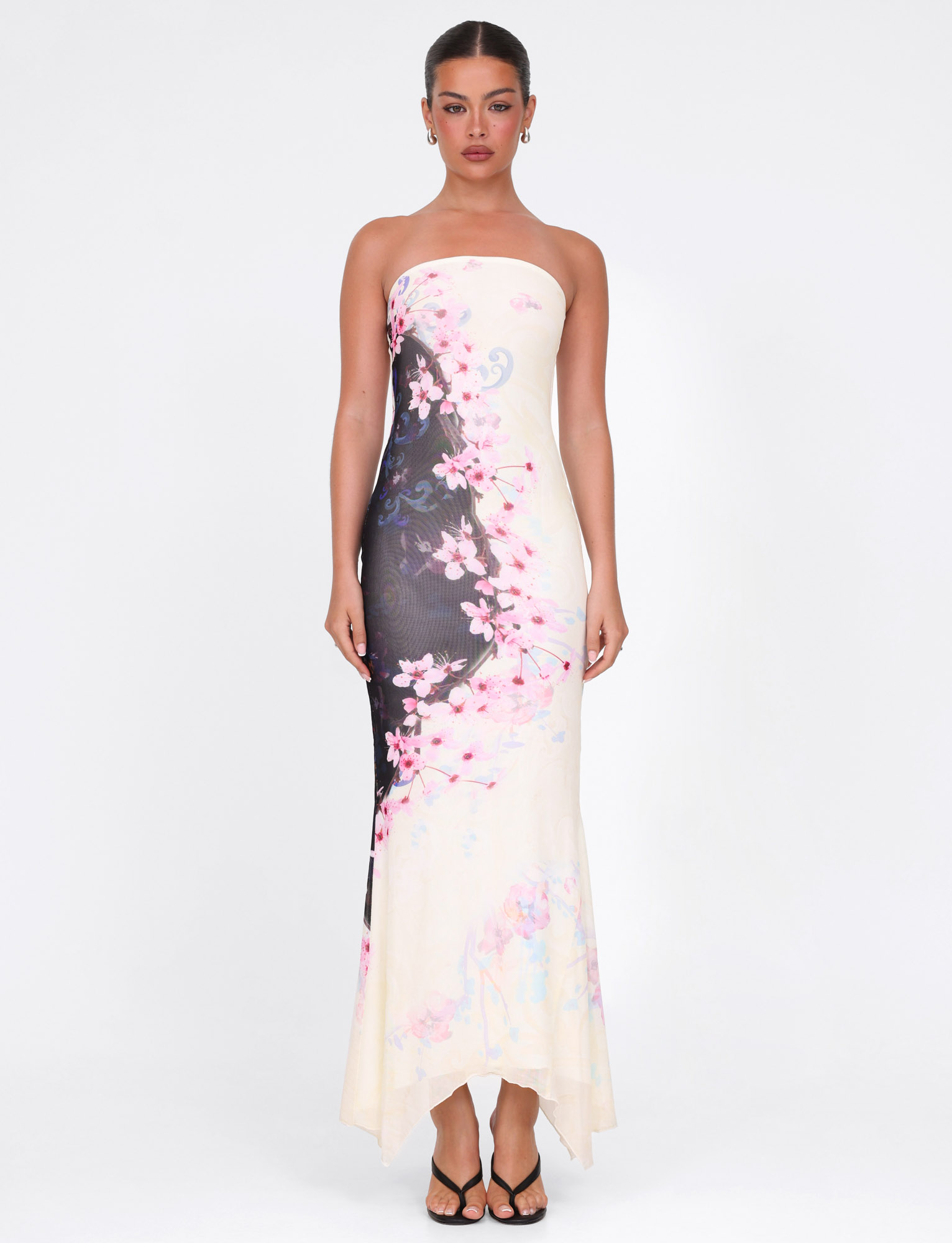 A woman faces forward in the TIGERMIST LILLIAN MAXI DRESS – MULTI: FLORAL: CHERRY BLOSSOM, a strapless high stretch mesh dress with a pink floral print, styled with black heeled sandals against a white background.