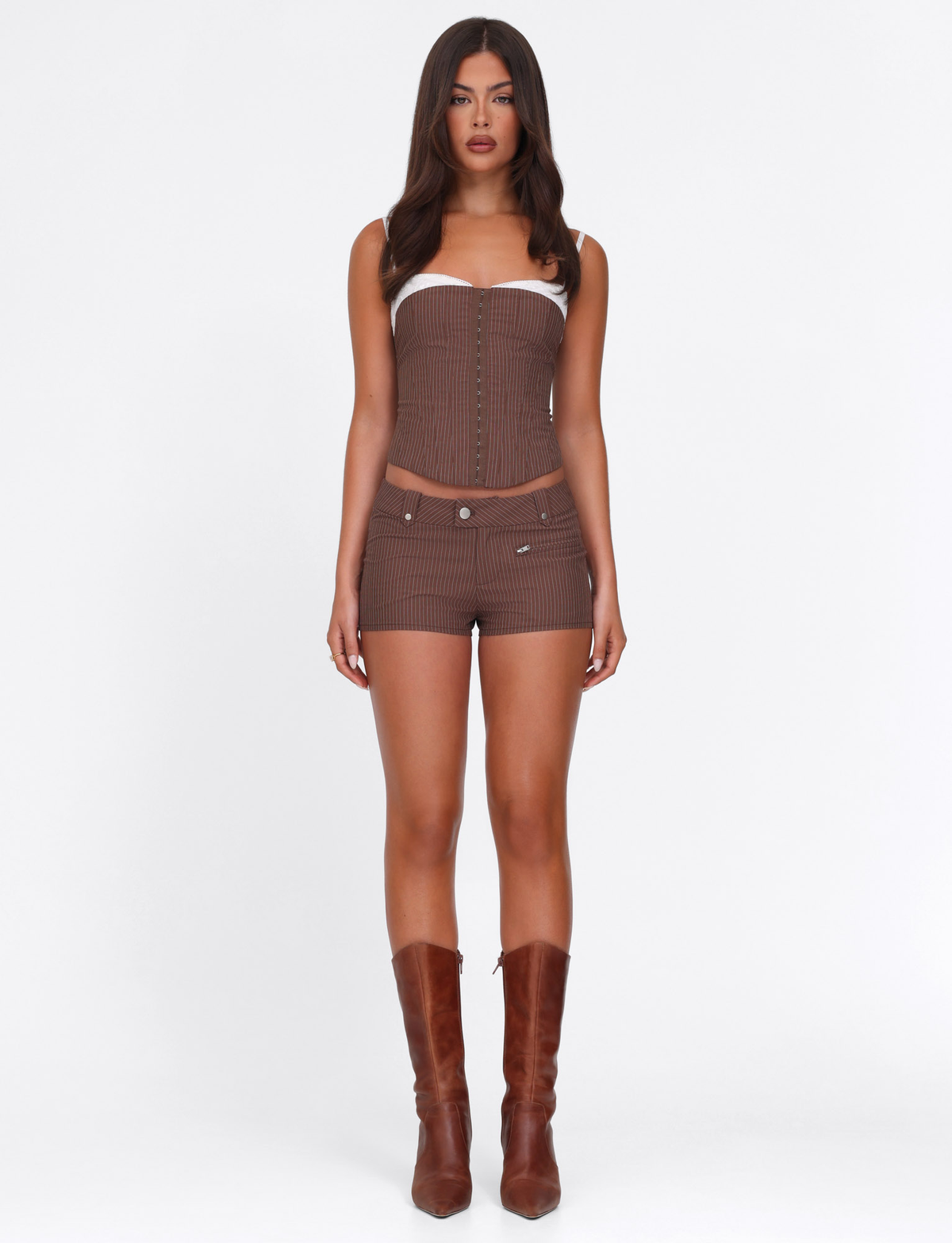 A woman faces forward wearing the TIGERMIST ANTONELLA SHORT in chocolate pinstripe with a matching strapless corset top and knee-high brown boots, posed against a plain white background.