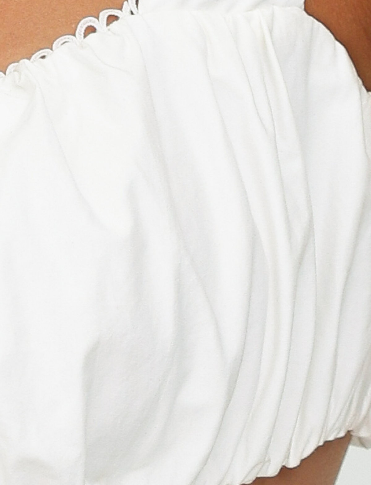 Close-up of a person wearing the TIGERMIST SABRA TOP in white, an off-the-shoulder cotton crop with ruched, gathered fabric. Only the upper chest, shoulder, and part of the arm are visible.