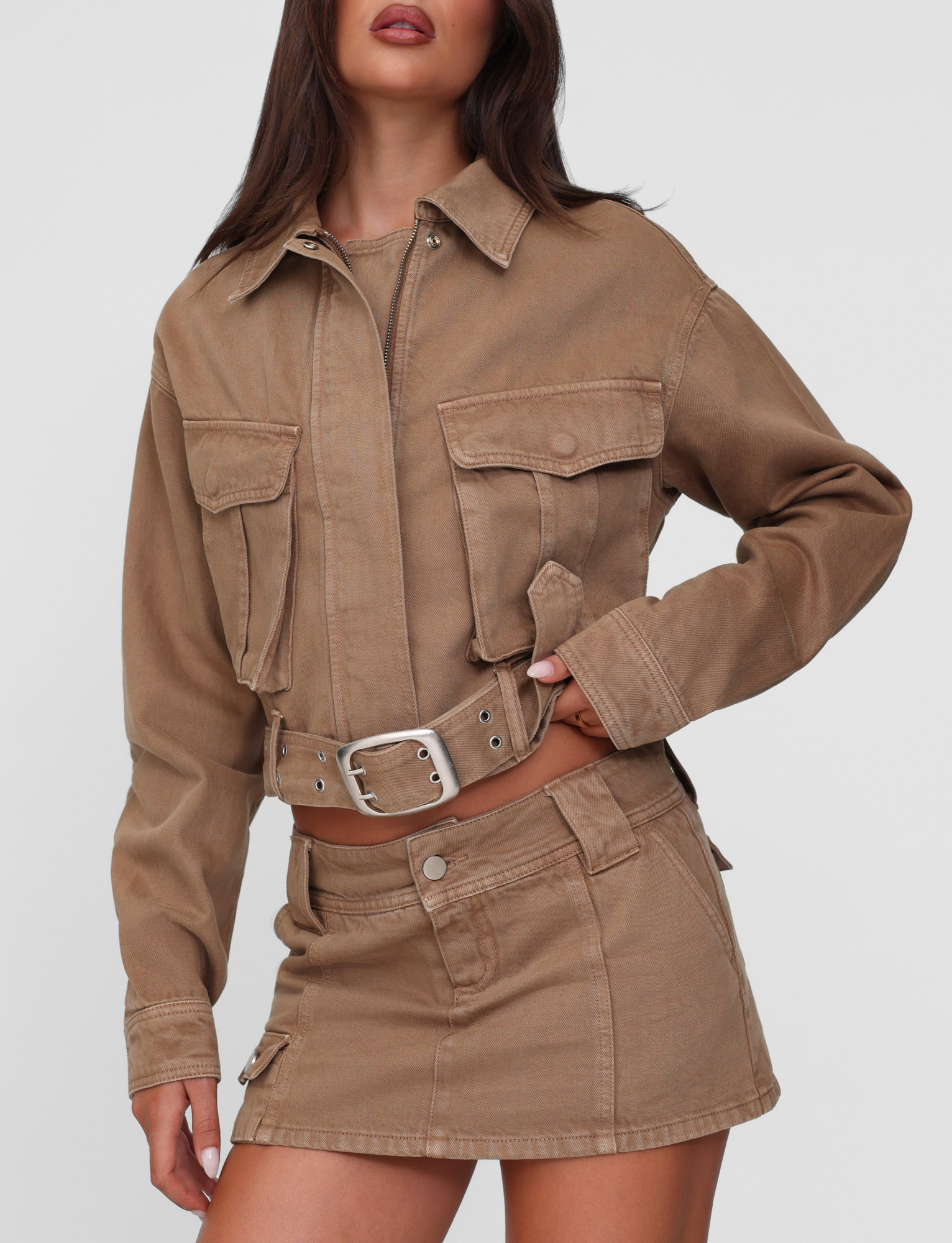 A woman wears the TIGERMIST ZELIE JACKET in washed tan with large patch pockets and silver buttons, paired with a matching mini skirt, set against a plain light background.