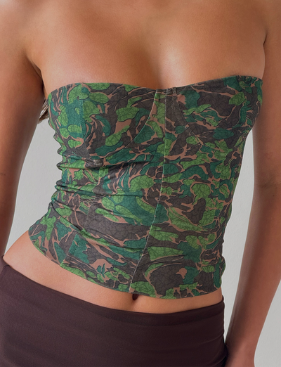 A person wears the TIGERMIST DULCE CORSET - GREEN : CAMO, a strapless fitted camo top, paired with a brown skirt against a plain light-colored background.