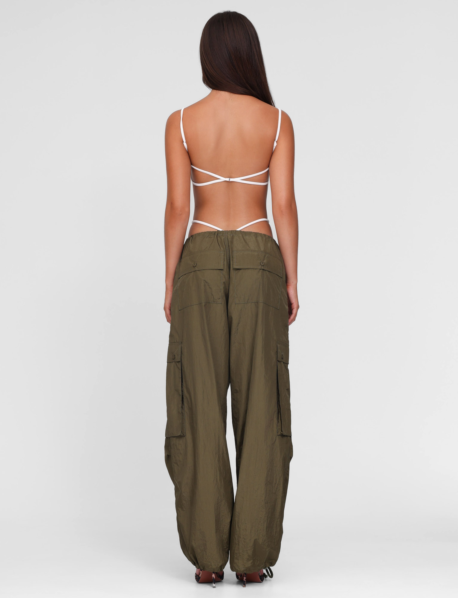 A woman faces away, wearing a strappy white open-back top and TIGERMIST VIOLETTE PANT in khaki green—loose, low-rise cargo pants with multiple pockets—against a plain light gray background.