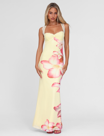 A woman wears the TIGERMIST NYOMI MAXI DRESS in Yellow Hibiscus macro floral print with lace straps and a lace bust panel, standing against a plain white background.