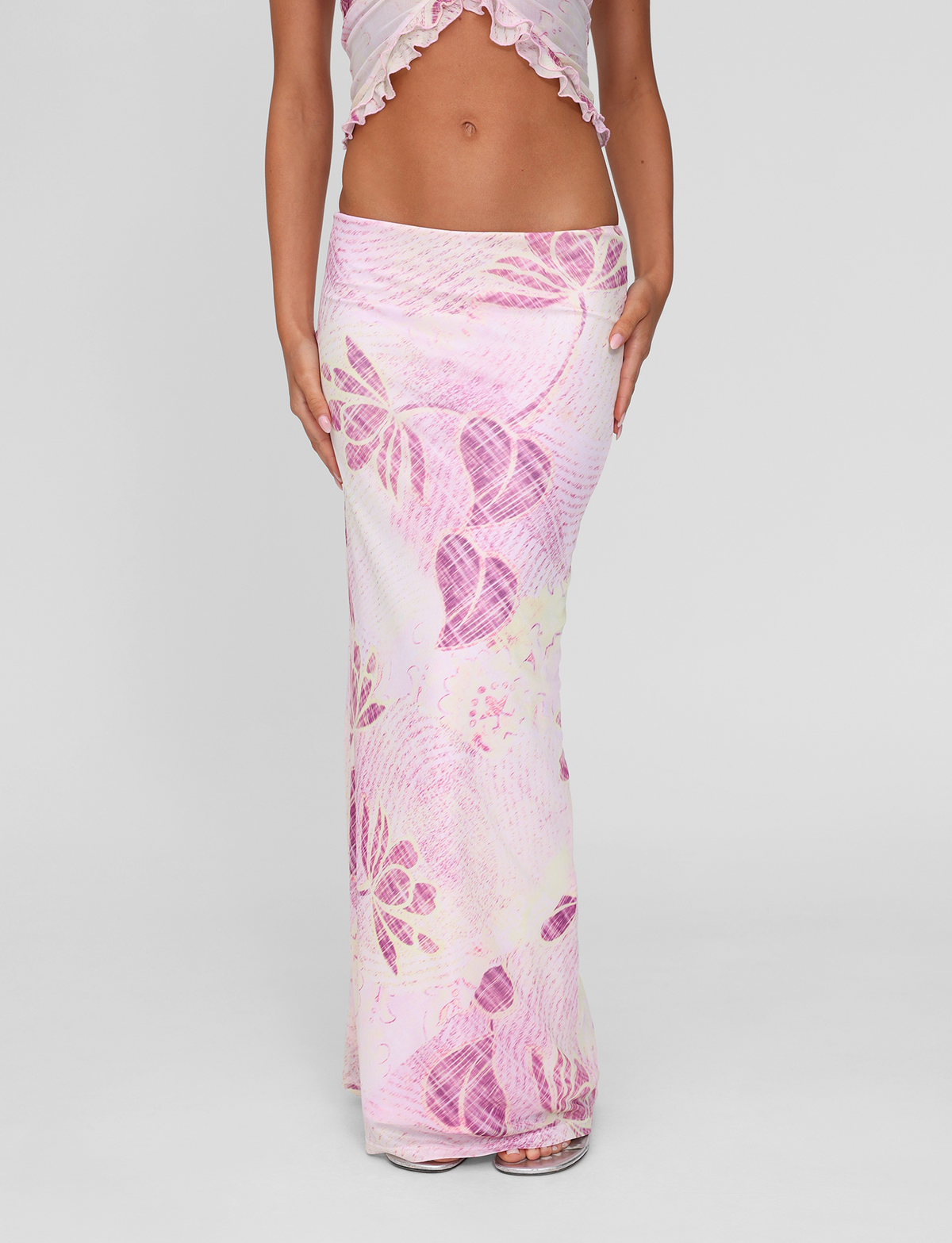 A person wearing the TIGERMIST DALILA MIDI SKIRT in Grunge Floral Magenta, paired with a matching cropped ruffled top, stands against a plain light gray background.