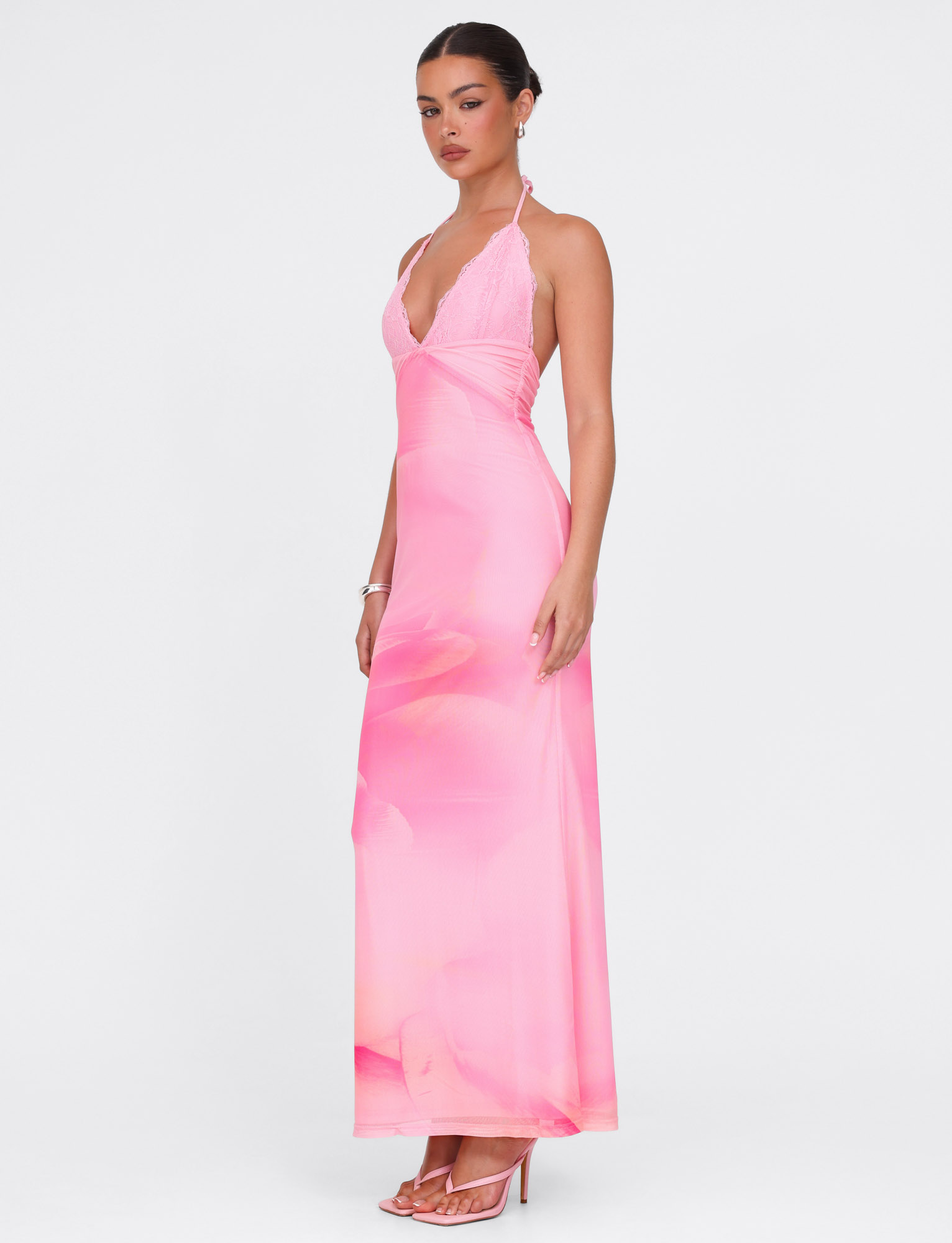 Woman wearing the TIGERMIST DENAE MAXI DRESS in Pink Blossom, a floral halter-neck maxi with deep V-neckline and open back, paired with heeled sandals against a plain white background.