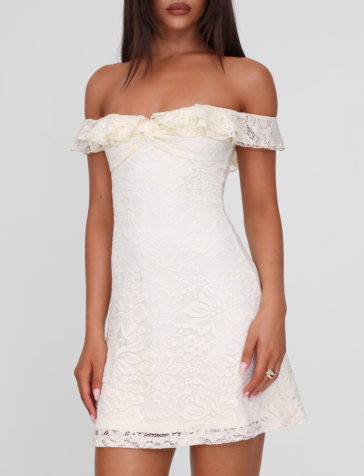 A woman wears the TIGERMIST DENALI LACE MINI DRESS in cream lace—an off shoulder mini dress with a ruffled neckline and fitted waist—standing against a plain light background.