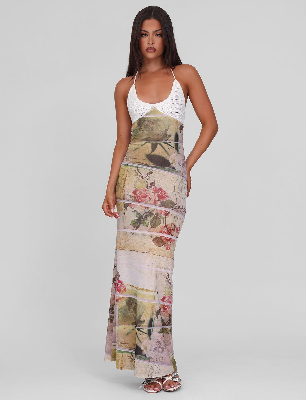 A woman with long, straight hair wears the TIGERMIST TILLEY MAXI DRESS - ROSE POSTCARD, featuring a fitted printed mesh, contrast crochet bust cups, and pastel floral skirt. She stands on a plain background in silver sandals.
