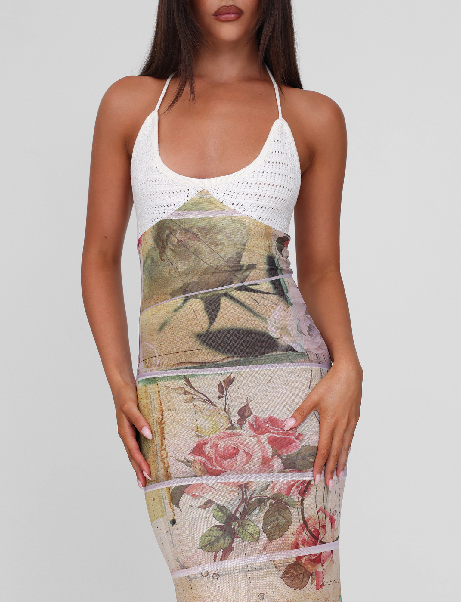 A woman wearing the TIGERMIST TILLEY MAXI DRESS - ROSE POSTCARD, featuring contrast crochet bust cups and a vintage rose floral print skirt, stands against a plain light gray background. Her face is partially out of frame.